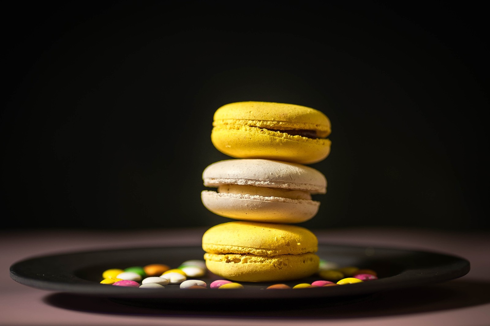 Há três macarons empilhados em um prato com doces. (macaron, sobremesa, cozimento, doces, bolo)