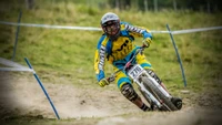 A mountain biker skillfully navigates a downhill course, showcasing speed and control against a backdrop of lush greenery.