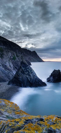 Des falaises majestueuses s'élèvent au-dessus d'une mer azur, encadrées par des nuages dramatiques et des eaux sereines.