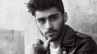 Black and white portrait of a cool male musician with a stylish hairstyle, facial hair, and intricate tattoos, conveying a thoughtful expression.