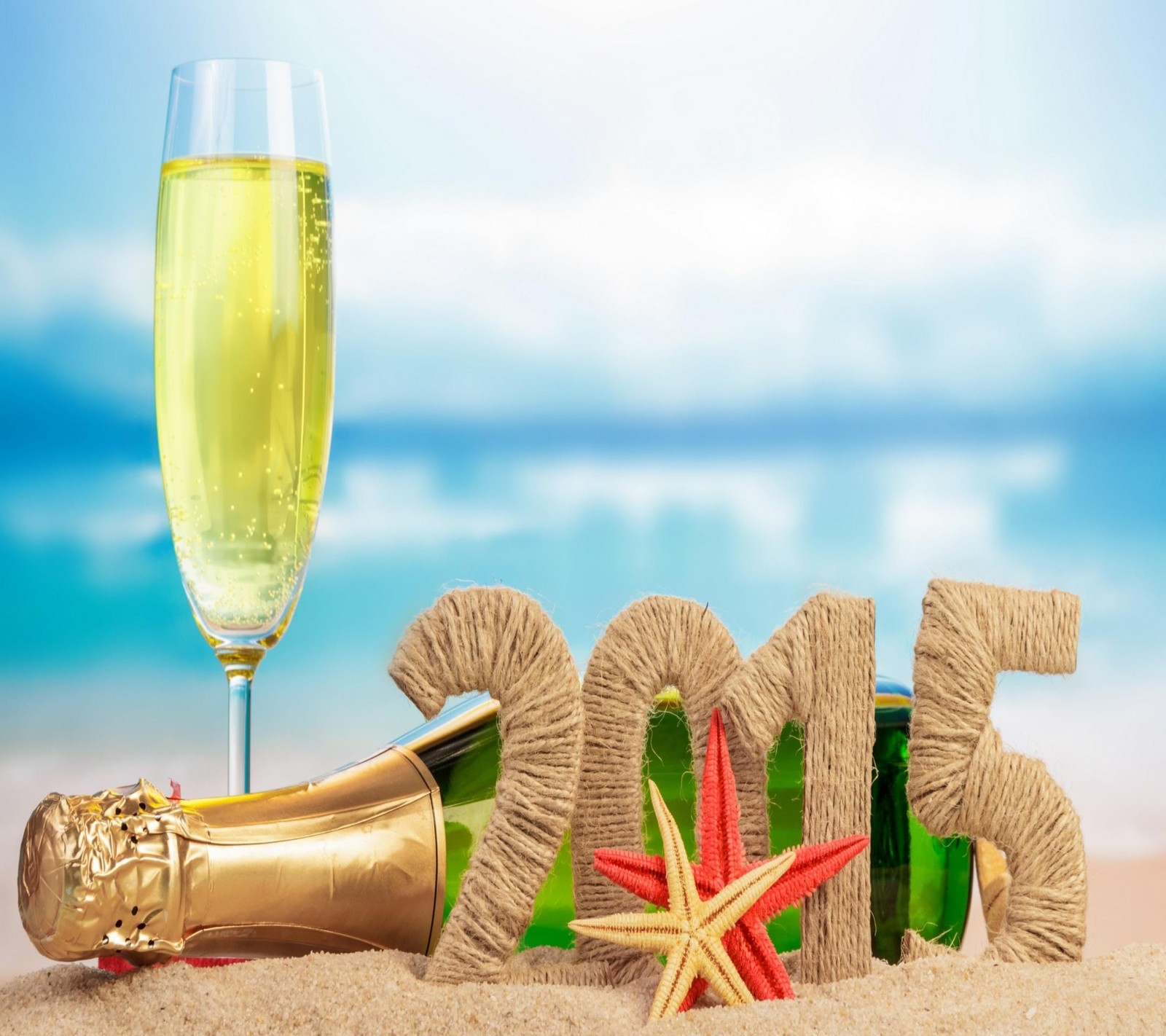 Nahaufnahme eines champagnerglases und einer flasche champagner am strand (2015, weihnachten, feuerwerk, gold, glücklich)