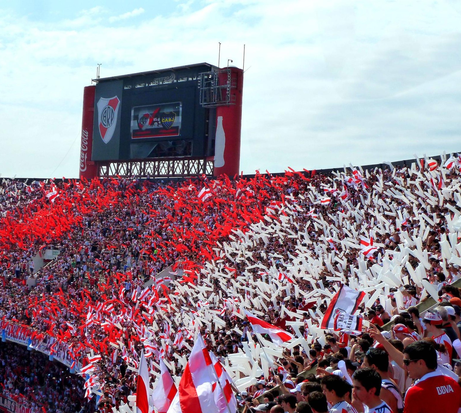 Multidão colorida de pessoas em um estádio com bandeiras e um grande painel (argetnina, futebol, futbol, river plate)