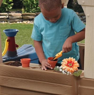 Kind beschäftigt sich mit Gartenarbeit mit Blumentöpfen im Spielbereich des Bauernhauses