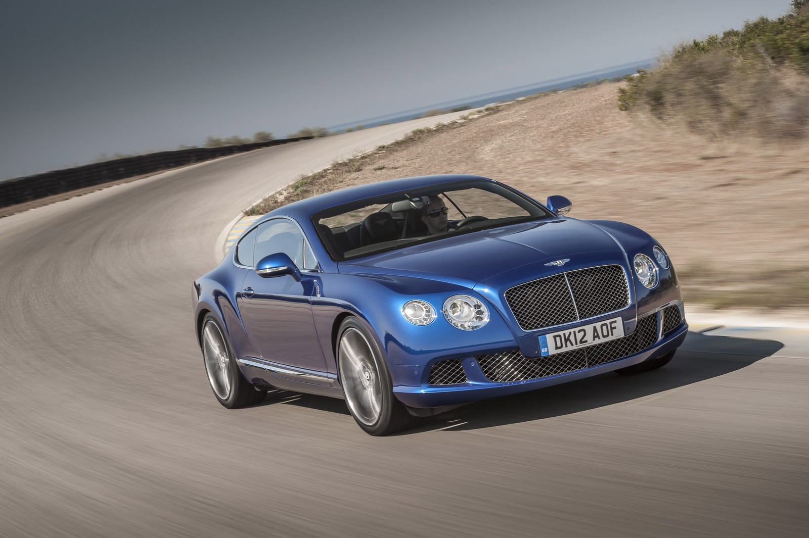 A blue bentley car driving down a road near a beach (bentley, bentley motors limited, car, bentley continental gt, bentley continental gtc)