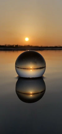 Reflejo del atardecer en una esfera de cristal sobre agua tranquila