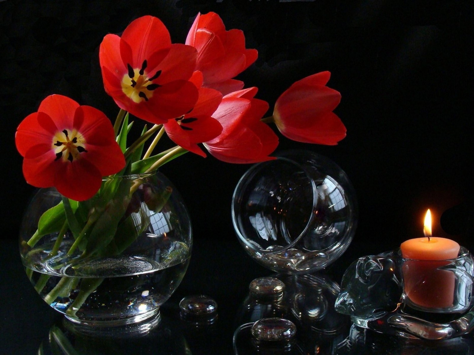 Il y a des fleurs rouges dans un vase et une bougie sur une table (pétale, bougie, verre, bouquet de fleurs, vase)