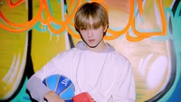 Jisung de NCT Dream tenant un ballon de basket devant un fond de graffiti vibrant.