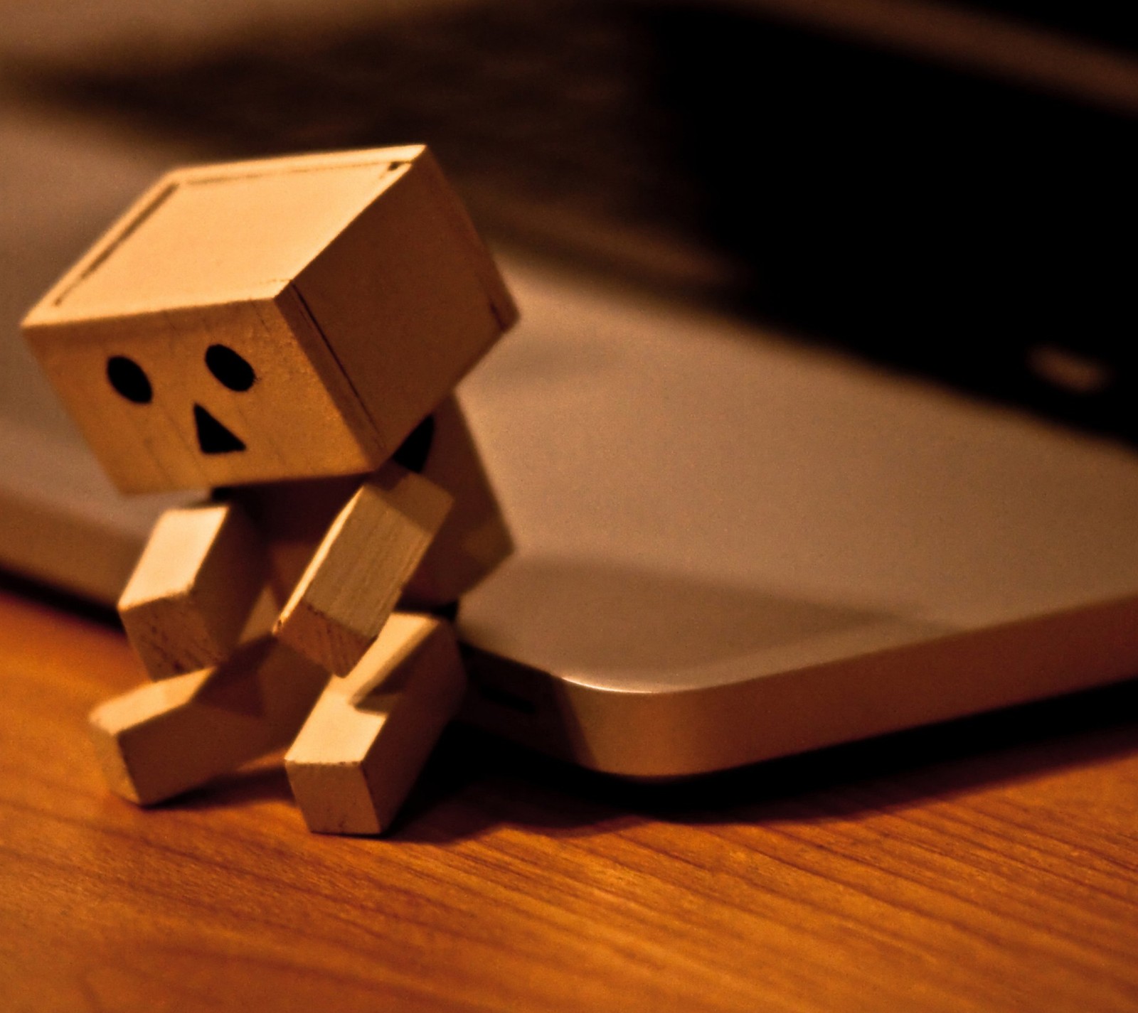 Il y a un petit robot en bois assis sur une table à côté d'un ordinateur portable. (seul, foreveralone, sad danbo, zedgevday)