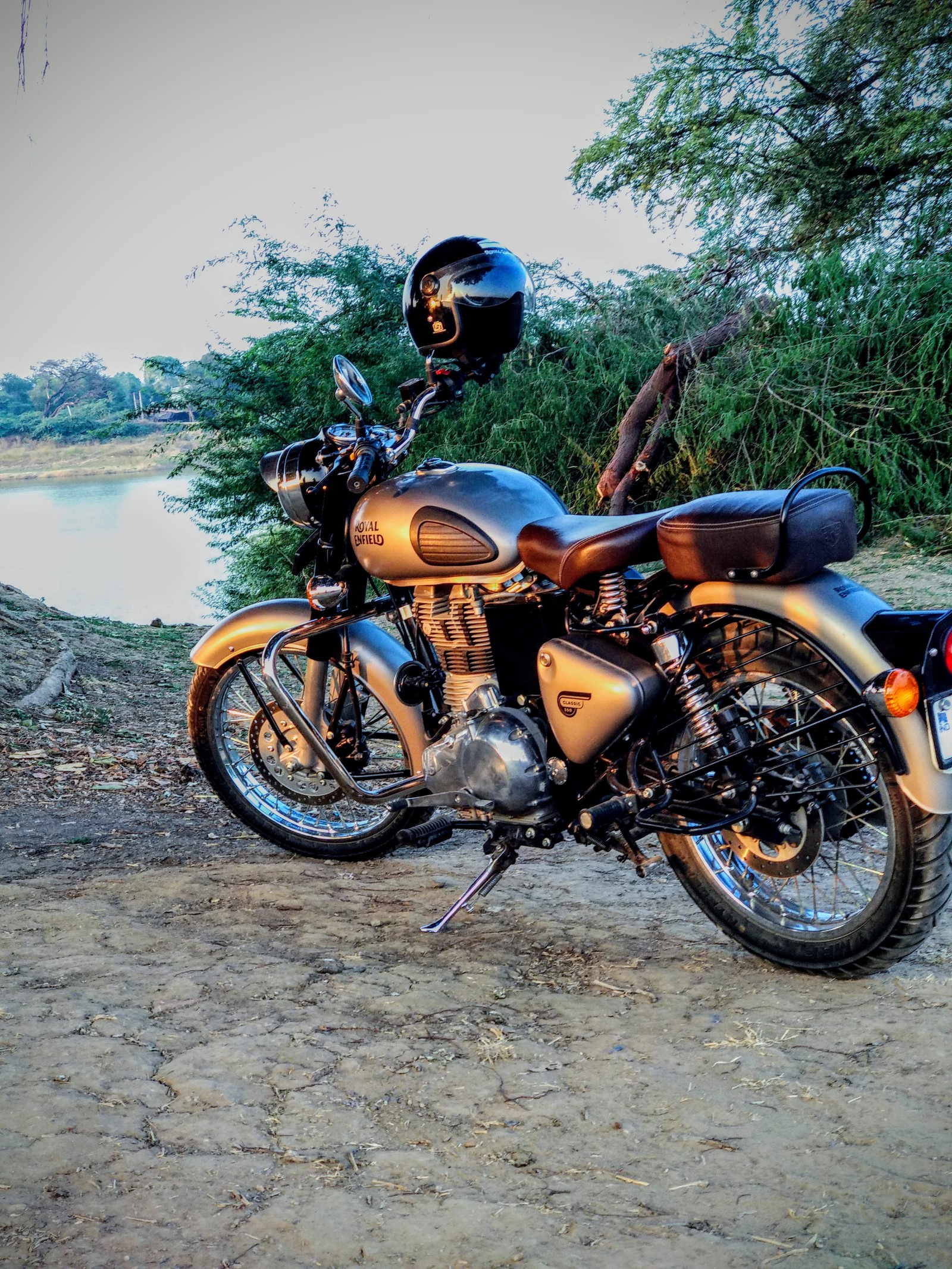 There is a motorcycle parked on the side of the road near a lake (adventure, bike, bullet, classic 350, indian bike)