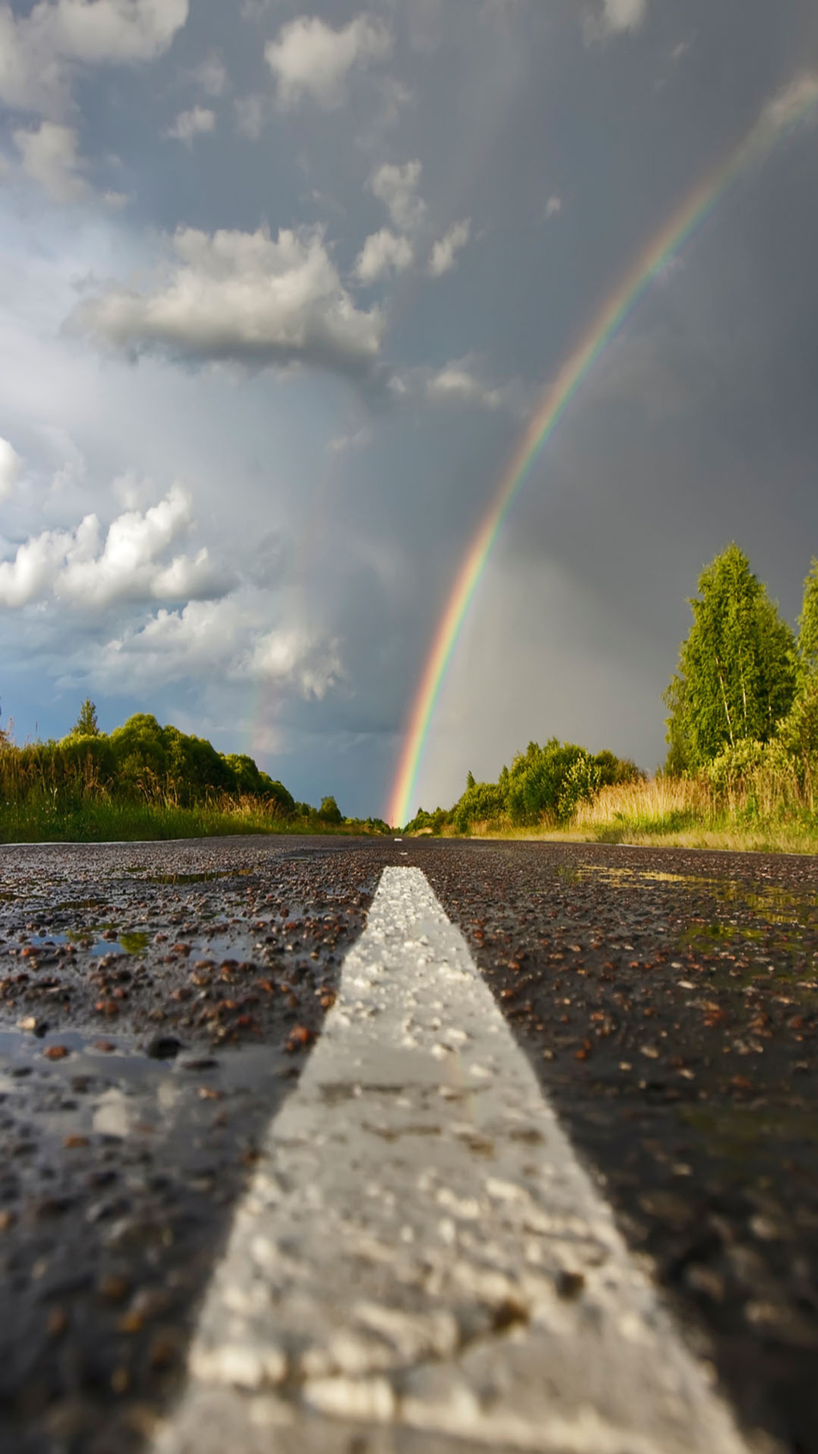 There is a rainbow in the sky over a road with a white line (bow, rain)