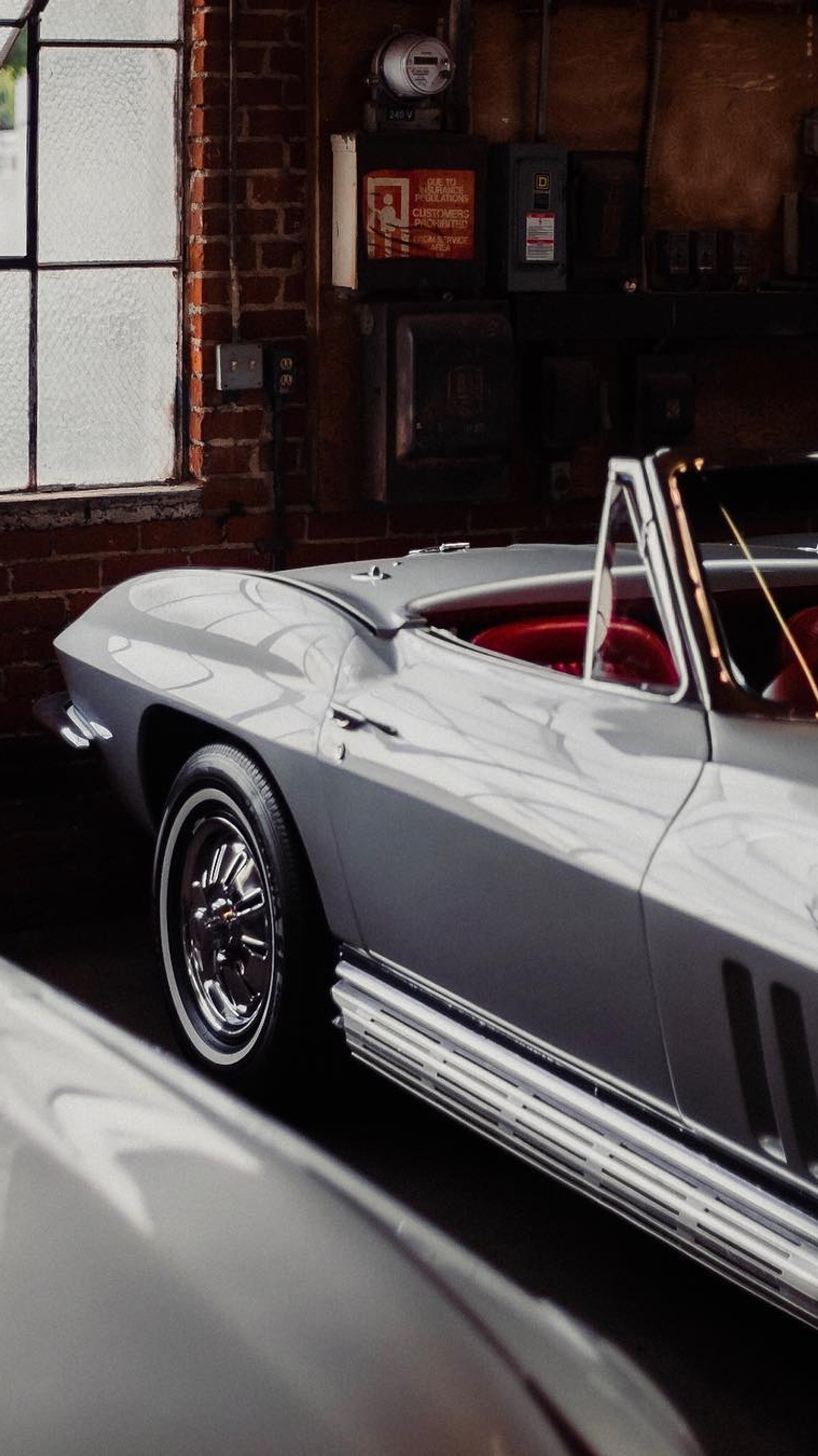 There is a silver corvette car parked in a garage (hood, cars, wheel, vintage car, convertible)