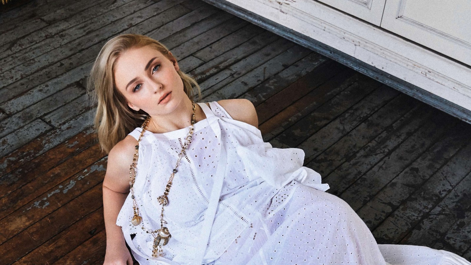 Femme arafed en robe blanche assise sur un sol en bois avec des colliers (sophie turner, actrice, célébrité, femmes, filles)