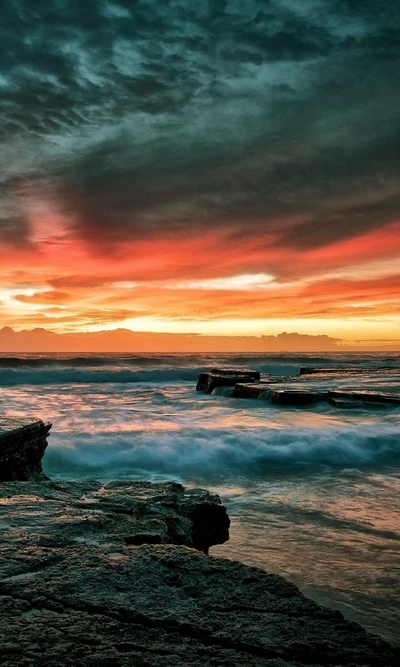 Pôr do sol vibrante sobre a costa rochosa com ondas do oceano