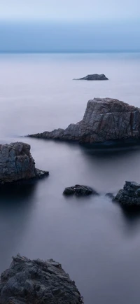 Ruhige Küstenlandschaft mit glattem Wasser und zerklüfteten Felsformationen bei Dämmerung.