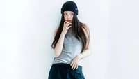 Hyein de New Jeans posando con estilo en un atuendo casual con un gorro, exudando confianza y encanto.