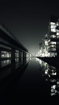 Moderne Stadtlandschaft bei Nacht, die sich in ruhigem Wasser spiegelt.