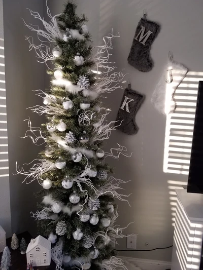 Elegante árbol de Navidad blanco adornado con adornos plateados y acentos decorativos, situado frente a una pared con medias navideñas.