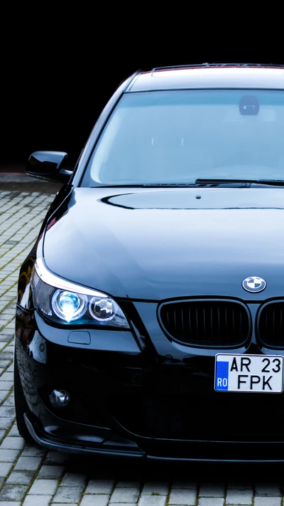 BMW M5 E60 in sleek black with striking headlights, parked on cobblestone.