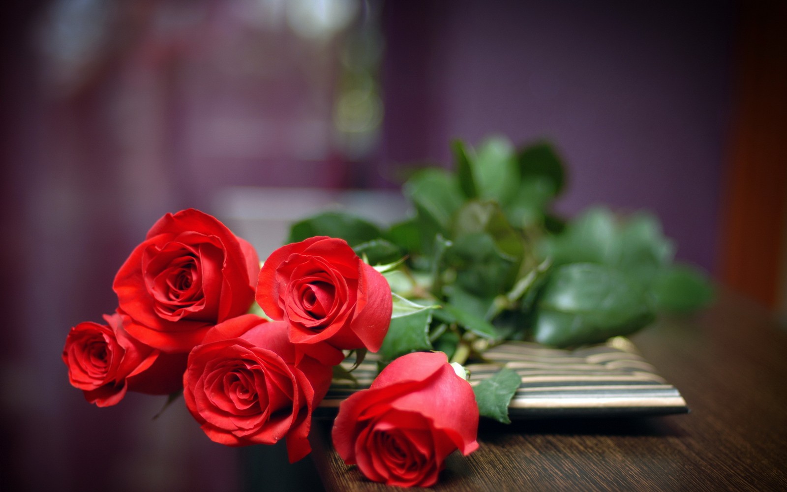 Il y a quatre roses rouges posées sur une table à côté d'un vase. (rose, fleur, roses de jardin, rouge, fleurs coupées)