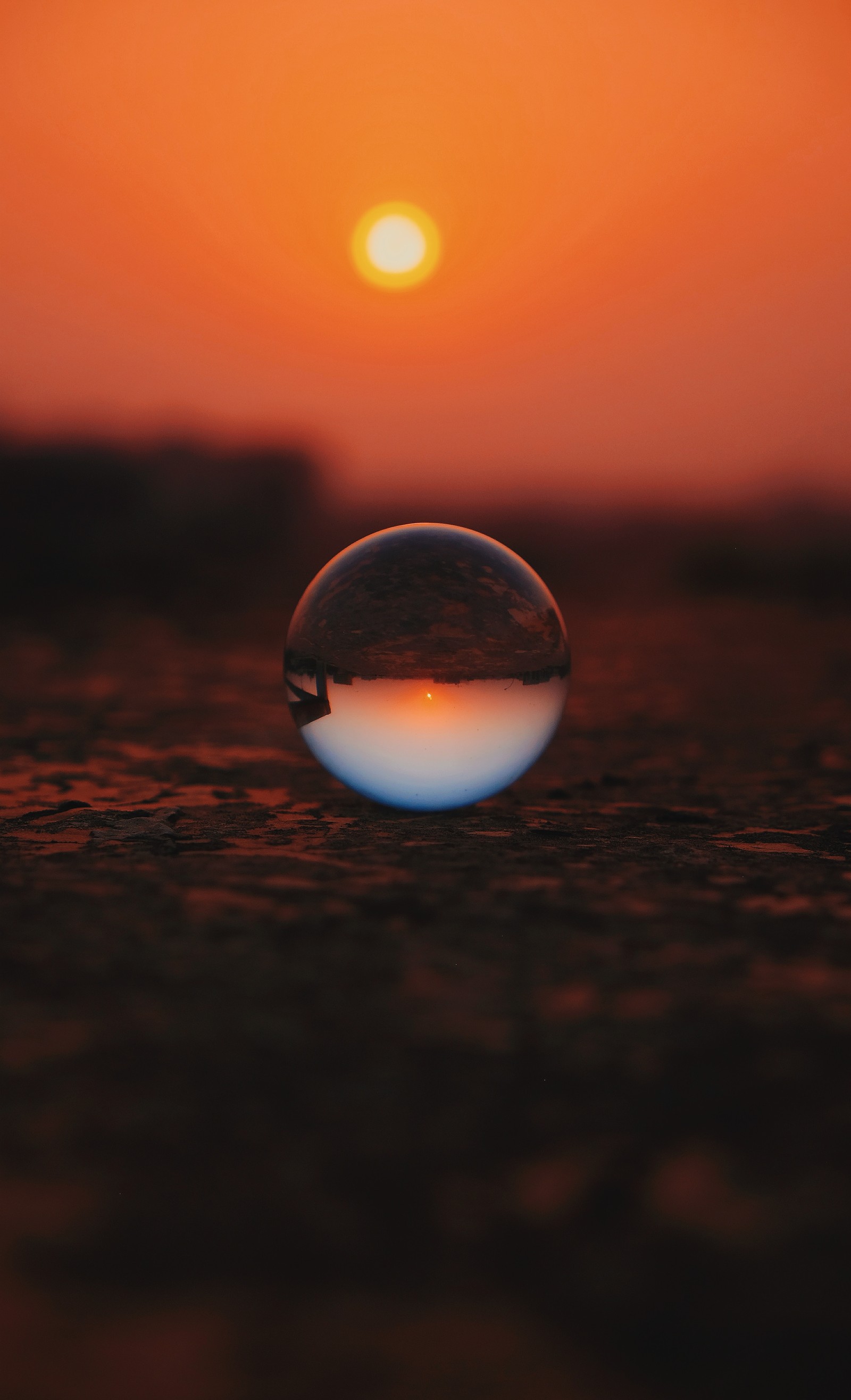 A close up of a glass ball on a ground with the sun setting in the background (reflection, water, sunset, calm, cloud)