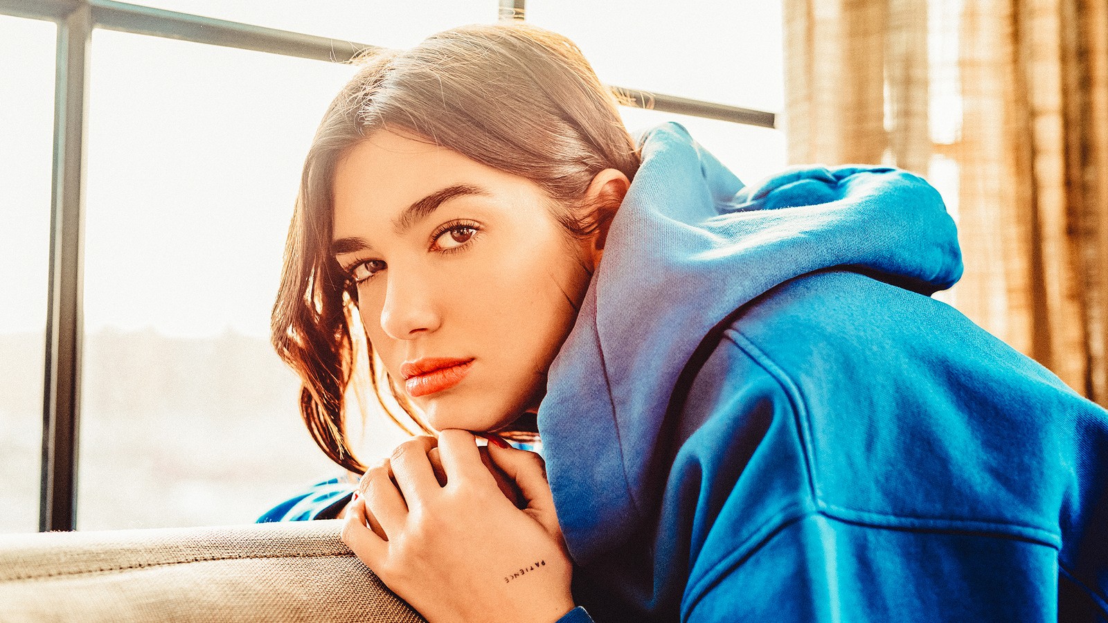 Arafed woman in blue hoodie leaning on a couch (dua lipa, singer, celebrity, girl)