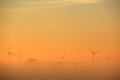 Sonnenaufgang über Windturbinen in einem nebligen orangefarbenen Himmel