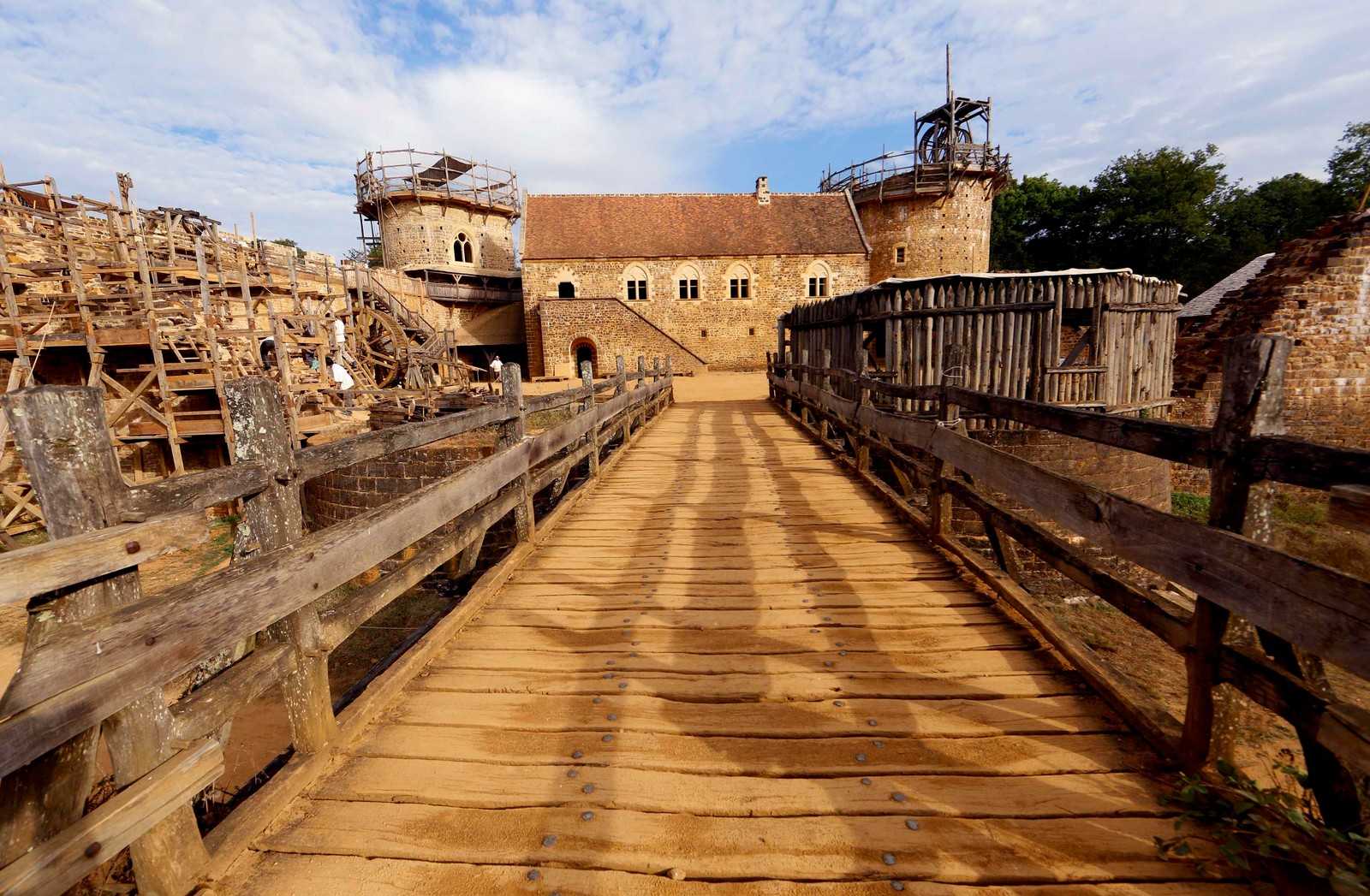 Arafed wooden walkway leading to a building with a tower in the background (castle, ancient history, building, fortification, historic site)