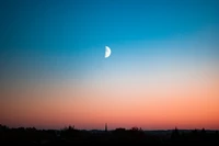 Media luna elevándose sobre un colorido horizonte al atardecer