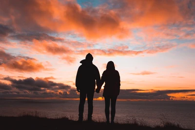 Casal em silhueta de mãos dadas ao pôr do sol à beira do oceano