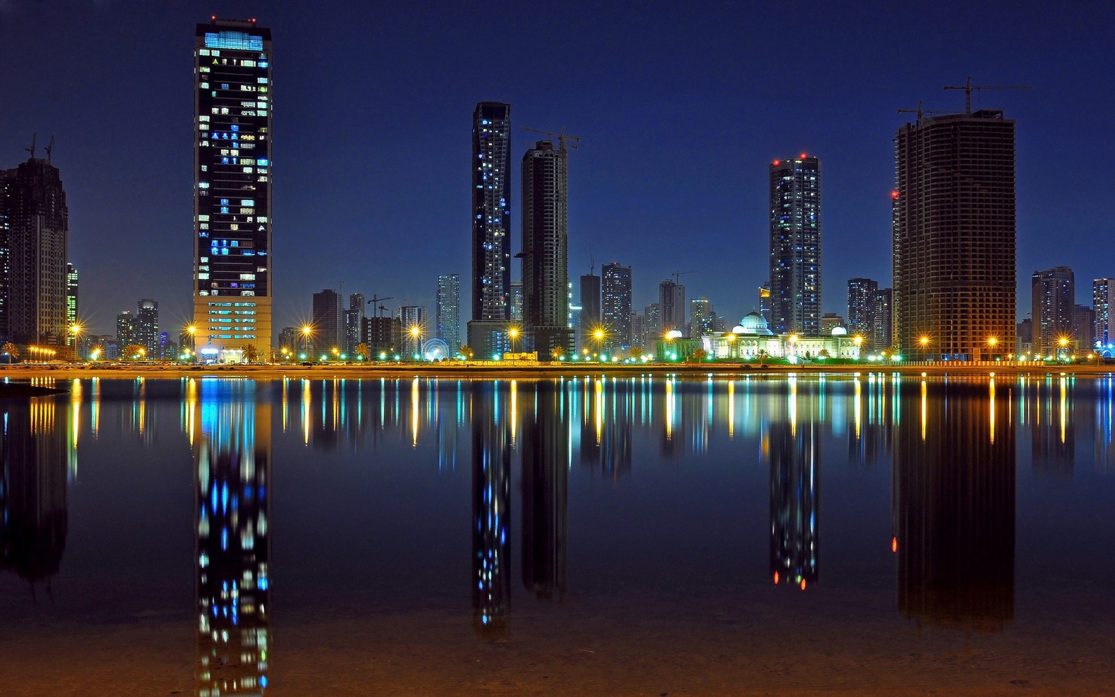 Vista desfocada de uma cidade à noite com um lago e edifícios (paisagem urbana, arranha céus, reflexo, cidade, linha do horizonte)