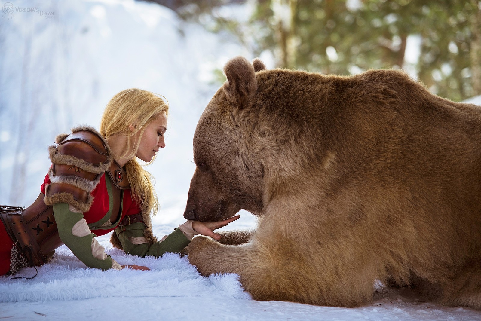 Blonde frau in winterkleidung streichelt einen großen braunen bären im schnee. (braunbär, grizzlybär, bär, schnee, wildleben)