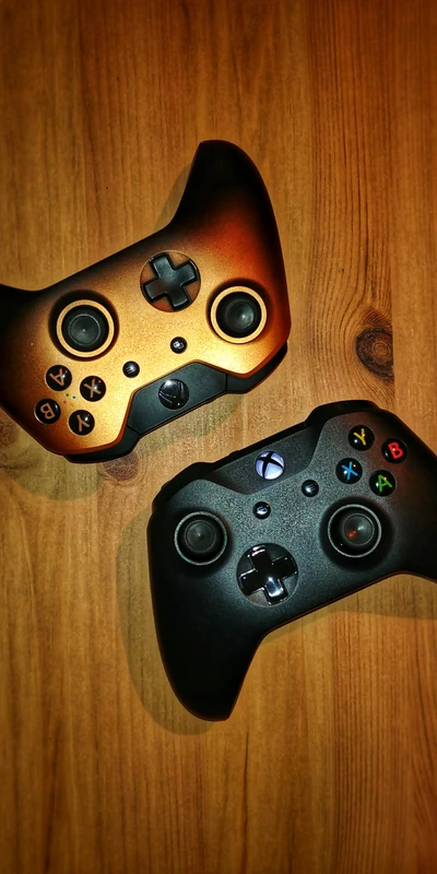 Deux manettes Xbox : or et noir sur une surface en bois