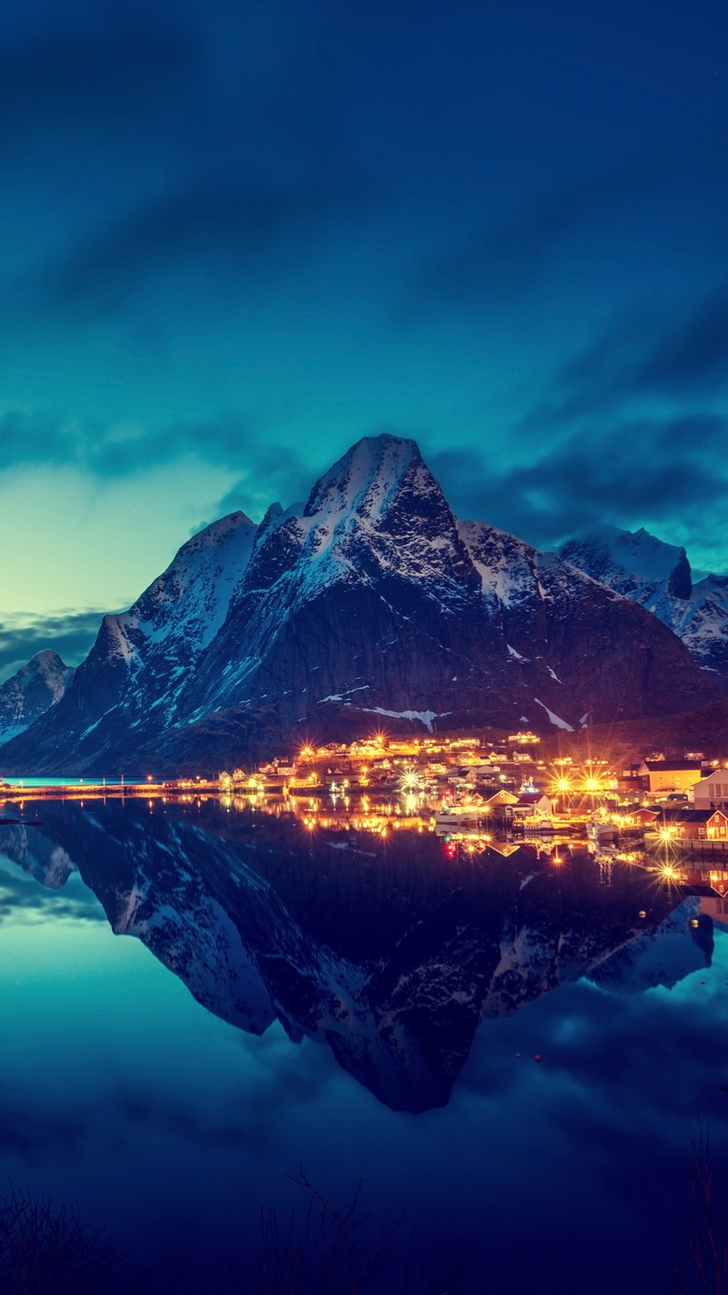 Montanhas refletidas em um lago à noite com uma cidade iluminada (montanha, noite, água)