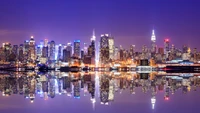 Vibrant night skyline of Manhattan reflecting on serene waters, showcasing skyscrapers and urban landmarks.