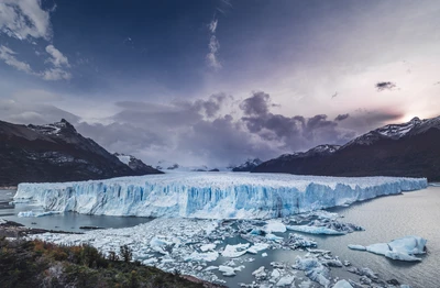 Glaciar majestuoso con vista a un sereno lago glacial entre nubes dramáticas y montañas cubiertas de nieve