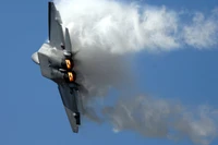 Lockheed Martin F-22 Raptor in flight, showcasing its stealth design and powerful afterburners against a clear blue sky.