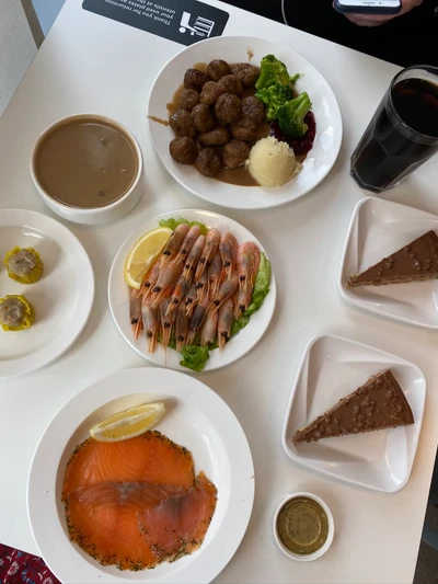 Una colorida presentación con un desayuno completo que incluye camarones, albóndigas, salmón ahumado y pastel de chocolate, servido en vajilla elegante.