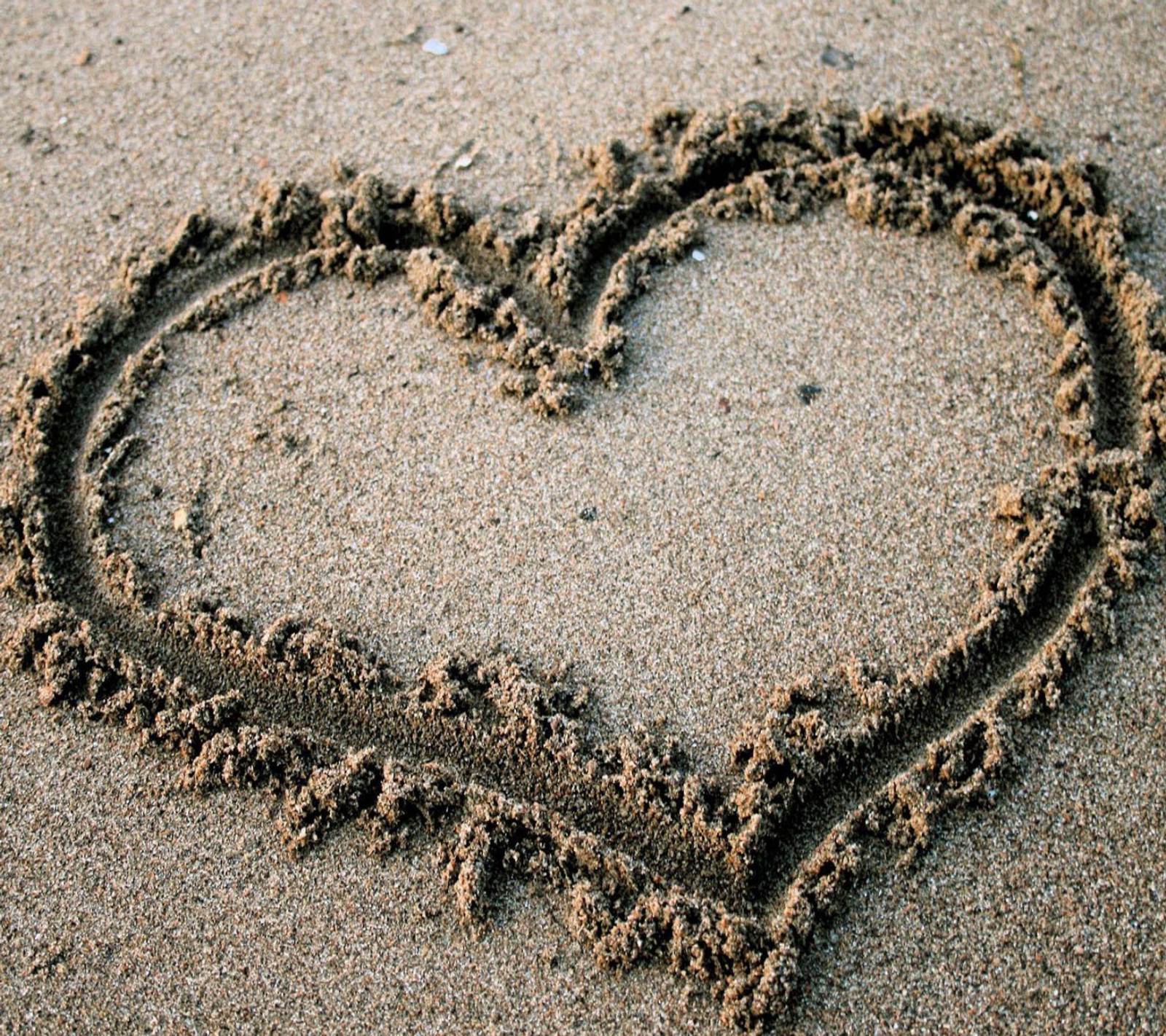 Un cœur dessiné dans le sable sur une plage (cœur)