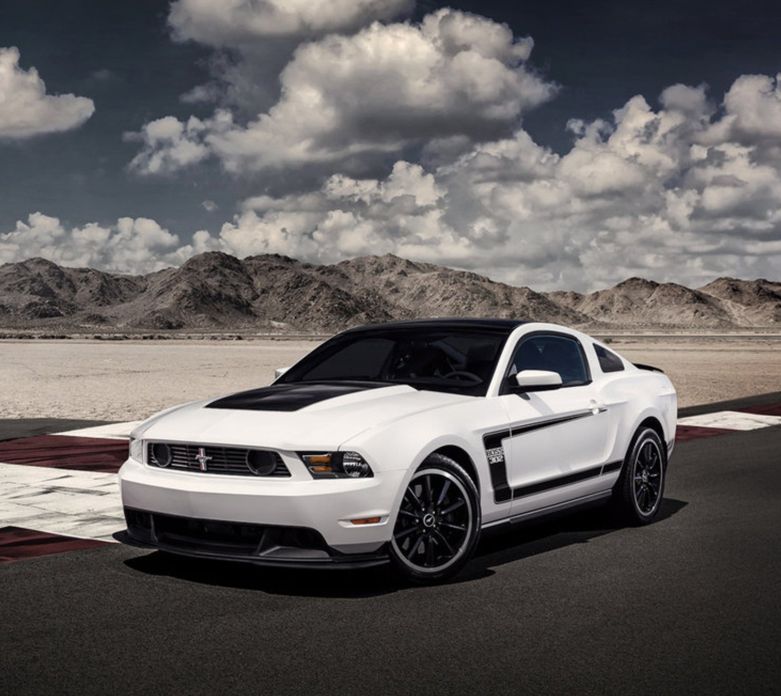 Une mustang blanche garée sur une piste de course avec des montagnes en arrière-plan (voiture, ford, mustang)