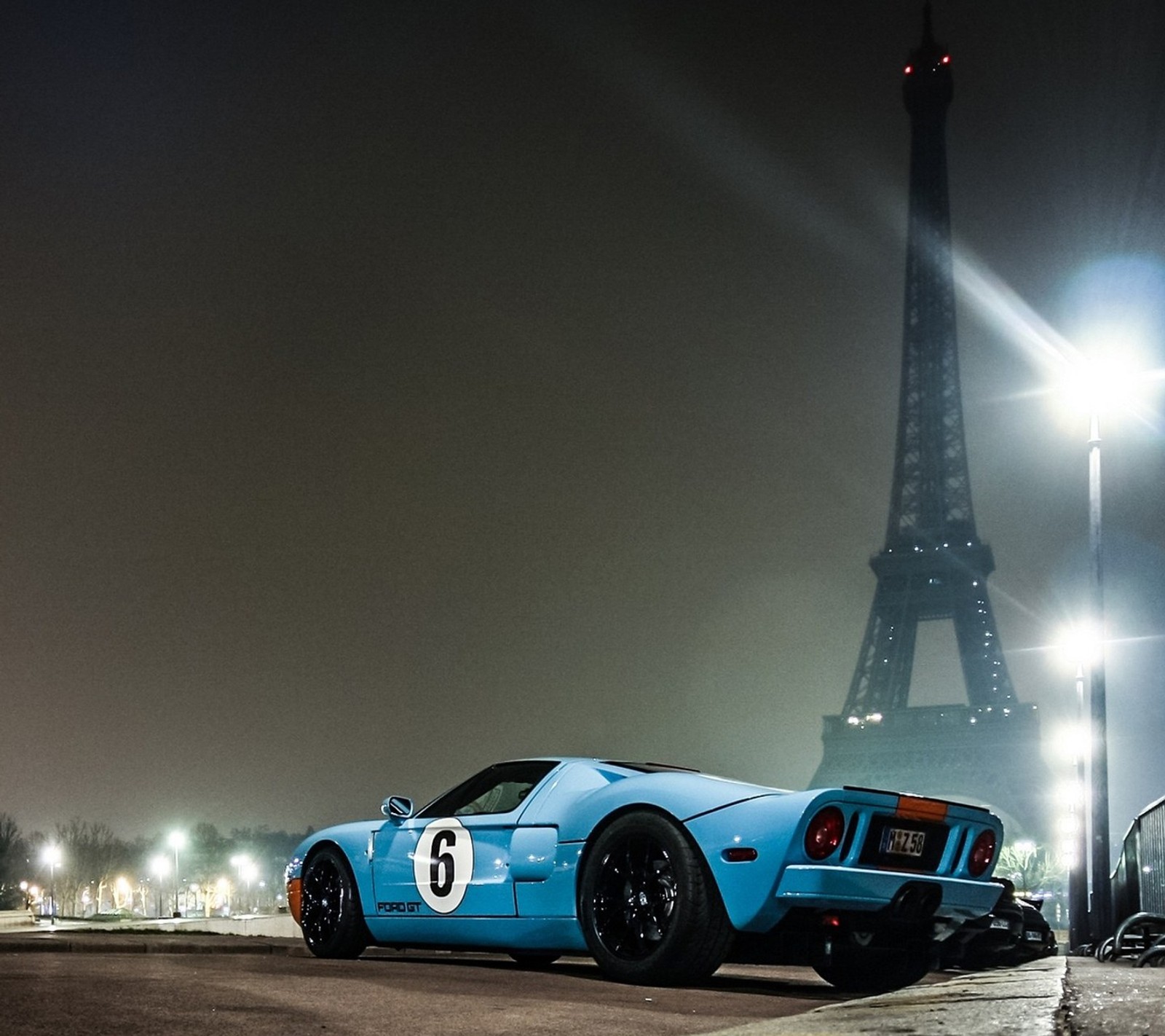 Un coche deportivo azul borroso estacionado frente a la torre eiffel (bue, coche, genial, rápido, ford)