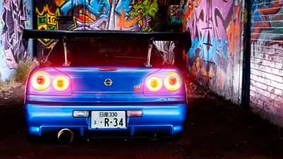 Nissan Skyline GT-R R34 в ярко-синем цвете, демонстрирующий свой культовый задний дизайн и смелый спойлер Nismo на фоне яркого уличного искусства.