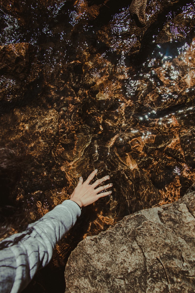 Кто-то тянется за камнем в воде. (скала, коричневый, геология, дерево, вода)