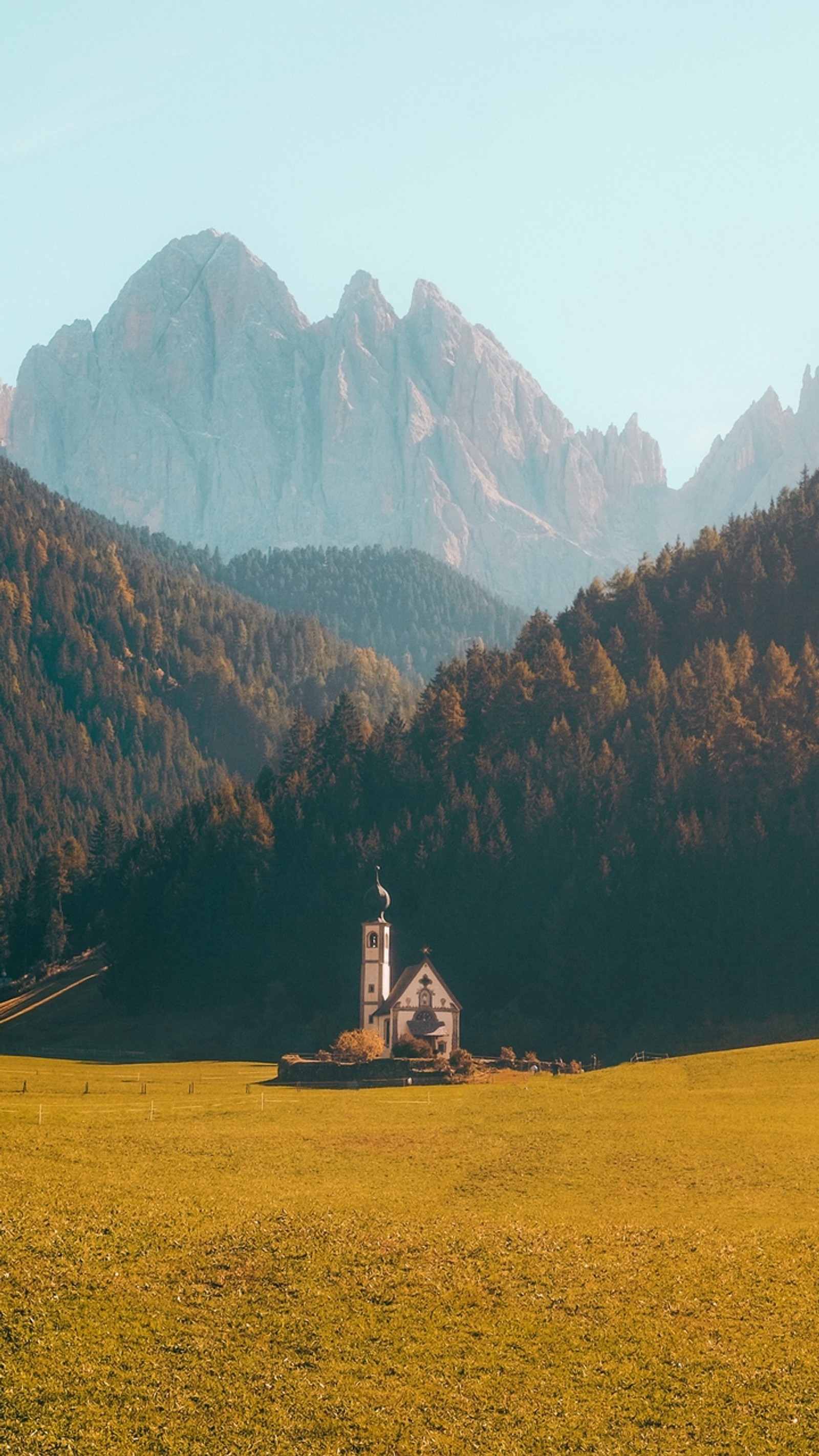 There is a large field with a house in the middle of it (dolomites, alps, building, mountain, plant)