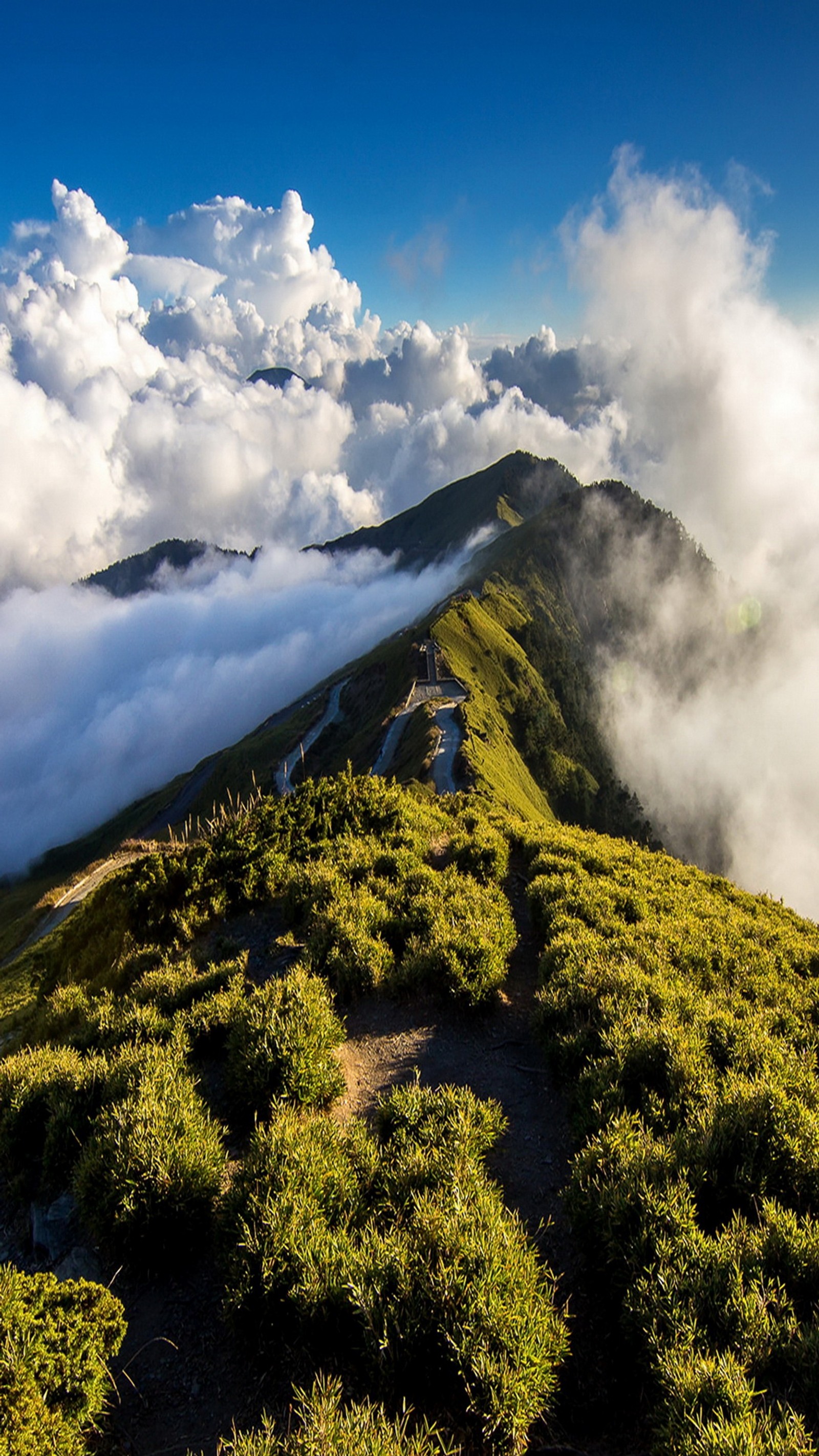 Il y a une montagne avec une zone herbeuse et quelques nuages (nuages, montagnes, chemin, ciel)