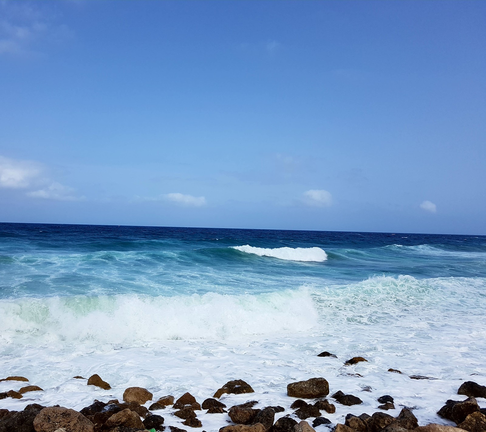 Una persona de pie sobre una tabla de surf en el océano (azul, naturaleza, rocas, s7 edge, mar)