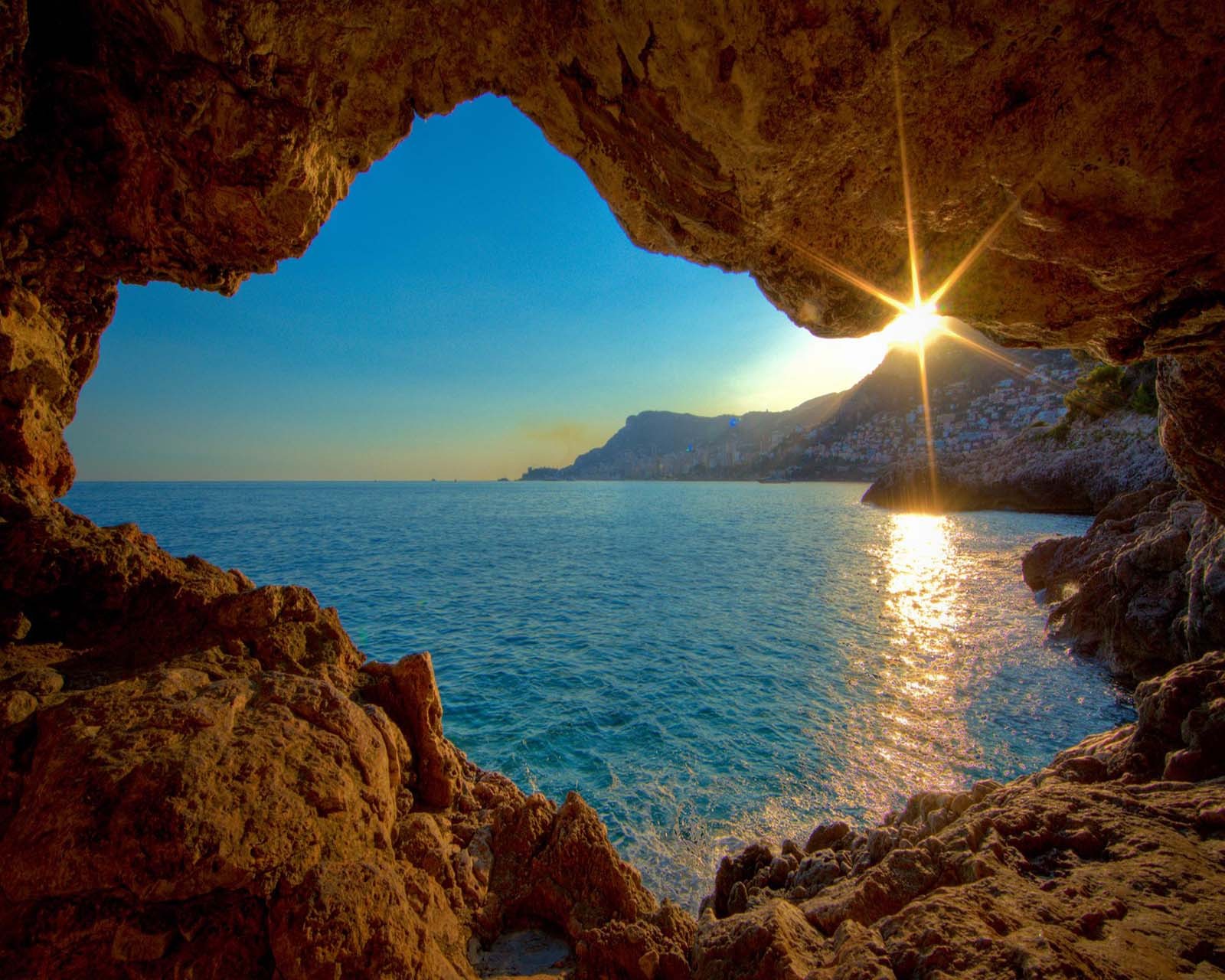 A view of the sun shining through a cave on the beach (cute, look, nice)