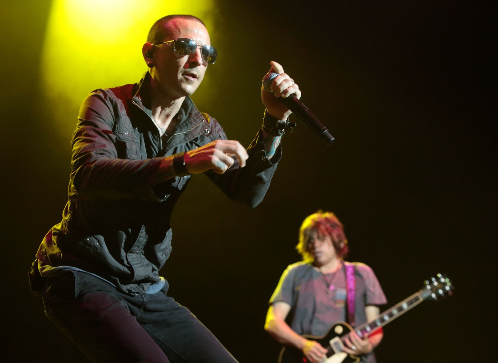 Arafed man in sunglasses and a black shirt holding a microphone and a guitar (guitarist, chester bennington, guitar, rock concert, linkin park)