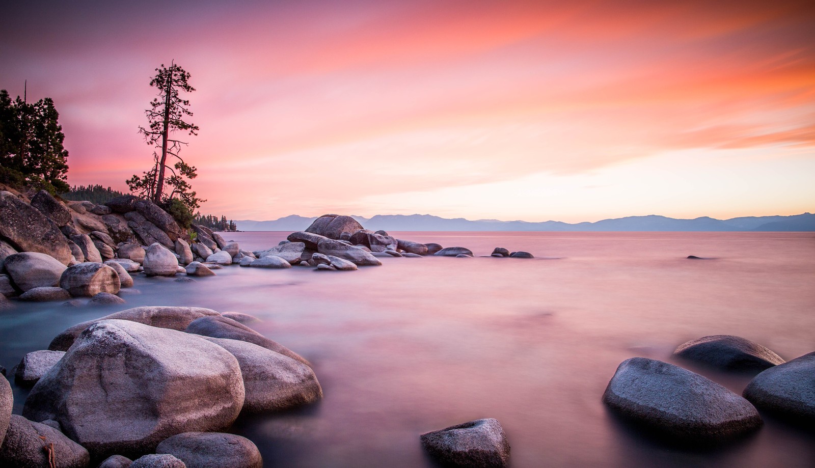 A long exposure photo of a sunset over the water and rocks (shore, sea, body of water, nature, natural landscape)