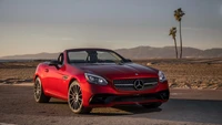 Cabriolet rojo Mercedes-Benz SLK con llantas elegantes contra un fondo de playa escénico.