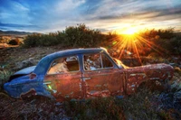 Sonnenuntergang über einem verrosteten klassischen Auto in einer ruhigen Landschaft